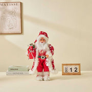 Red and white Christmas doll ornament with Santa Claus holding gifts on a table with calendar and books
