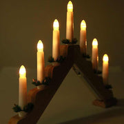 Wooden Christmas window decoration with seven lit candlesticks and green accents