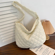 Cream-colored quilted warm totes shoulder bag with soft nylon material and zipper closure on wooden surface with lamp background