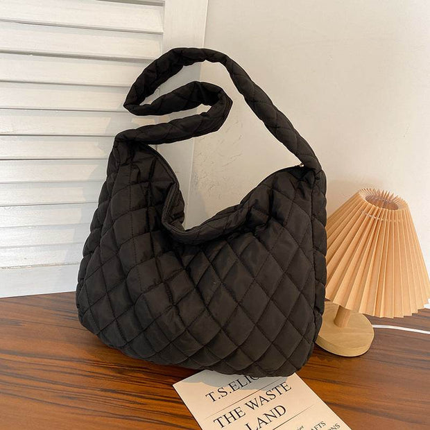 Black nylon warm totes shoulder bag with quilted design and soft handle on wooden table near lamp