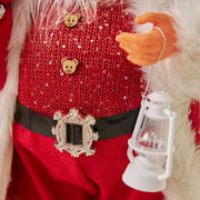 Close-up of Christmas doll ornament holding a white lantern, wearing red sequined outfit with bear buttons and decorative belt buckle