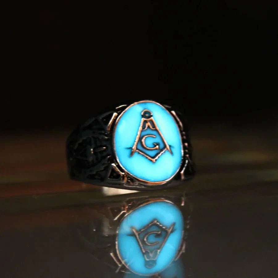 Glow ring with turquoise luminous Freemason symbol on metal band at night