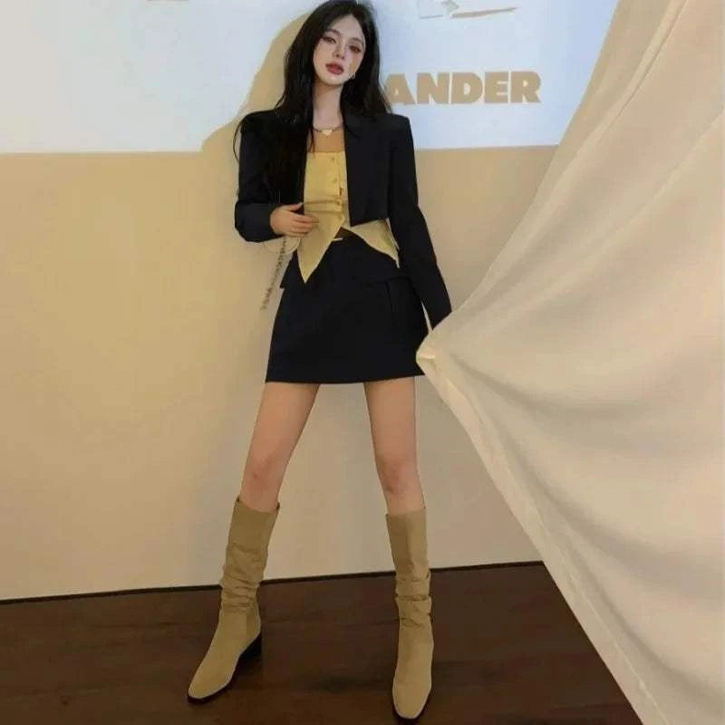 Elegant female outfit two-piece set with black long sleeve jacket and matching skirt paired with beige boots