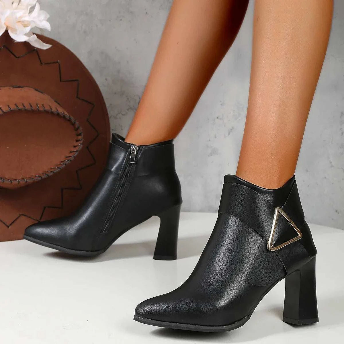 Black high-heeled women's ankle boots with pointed toe and decorative buckle, zip closure, and square heel design