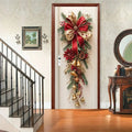 Christmas wall decoration with red bells, green leaves, pinecones, and a large red and gold bow hanging on a door