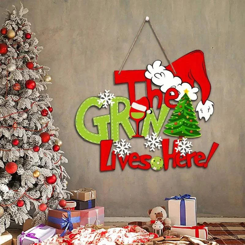 Christmas wall decoration with "The Grinch Lives Here" text, Santa hat, snowflakes, and festive colors near decorated Christmas tree and gifts