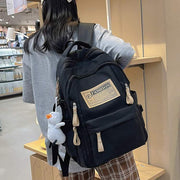 Black solid multi-pocket nylon backpack with pendant worn by a student in a school setting