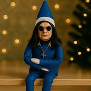 resin Christmas Oz Doll elf decoration in blue outfit with hat and sunglasses sitting on wooden surface with blurred warm lights background