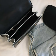 black fashion designer bag with diamond lock and compartments next to blue denim jeans and a black hat