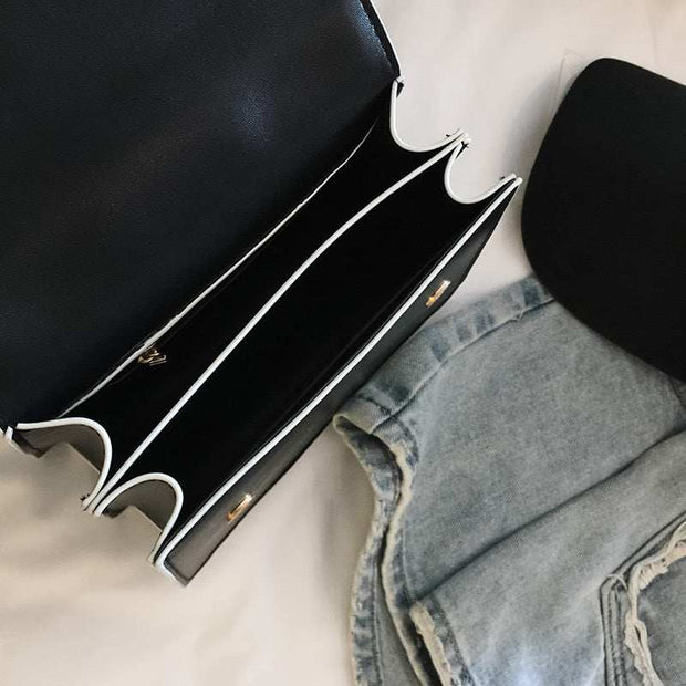 black fashion designer bag with diamond lock and compartments next to blue denim jeans and a black hat