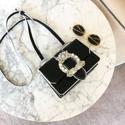 Black fashion designer bag with diamond lock and pearl embellishments on marble table with sunglasses