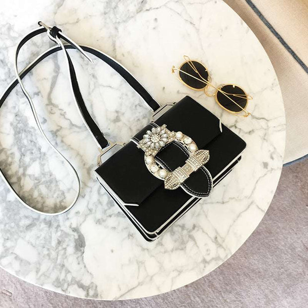 Black fashion designer bag with diamond lock and pearl embellishments on marble table with sunglasses