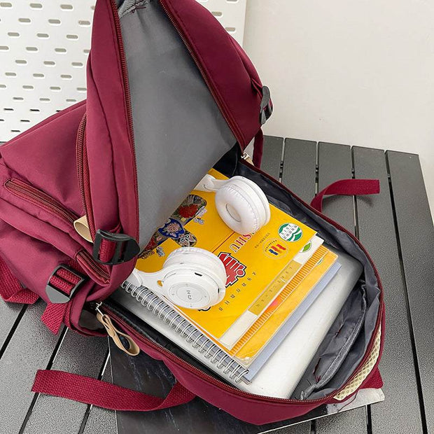 Solid multi-pocket backpack in burgundy with large capacity, open to show notebooks and white headphones inside.