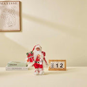 Christmas Doll Ornament in red Santa suit holding gifts, standing on table next to calendar showing December 12