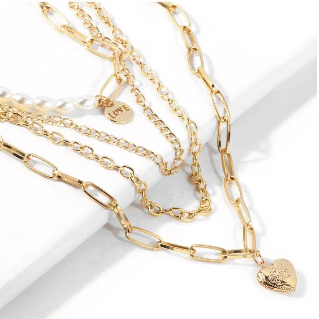 Jester Necklace featuring layered gold chains, pearls, and a heart pendant on a white surface.